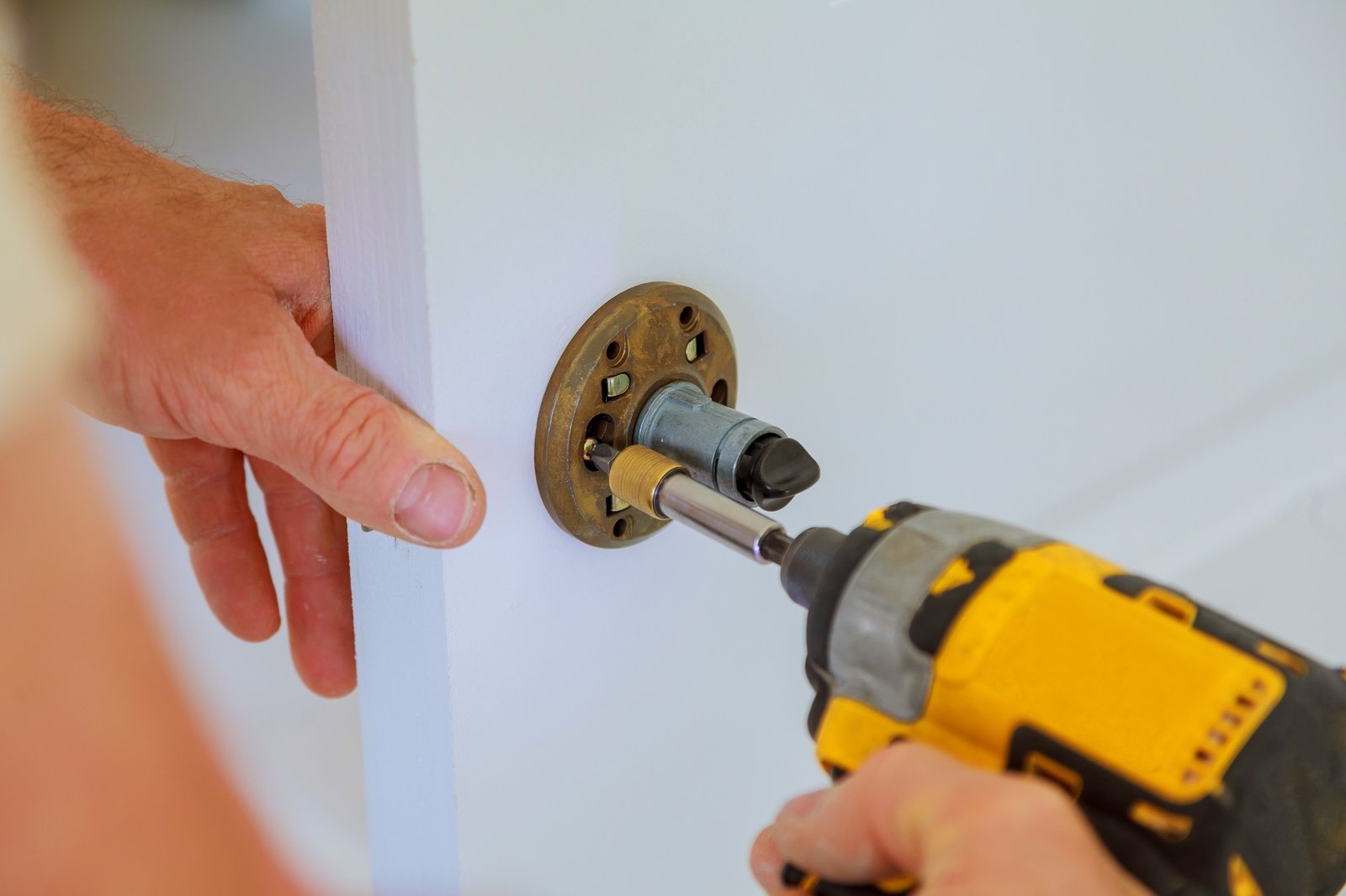 carpenter at lock installation with electric drill into interior wood door